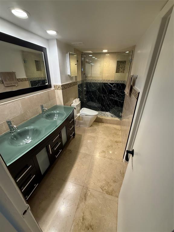 19428 Northeast 26th Avenue, Unit 103 Miami, FL 33180 - Photo 29 of 65 a bathroom with a large mirror vanity and toilet