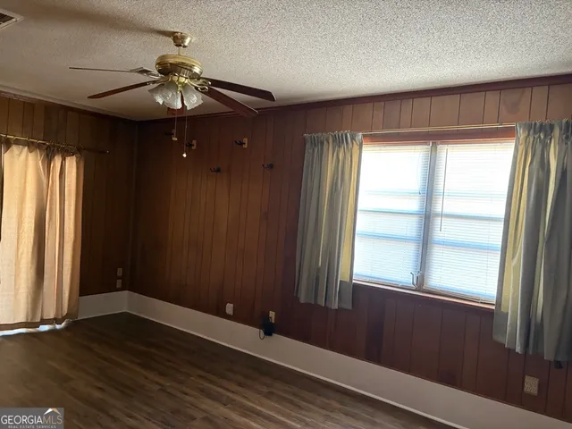 an empty room with wooden floor chandelier fan and windows