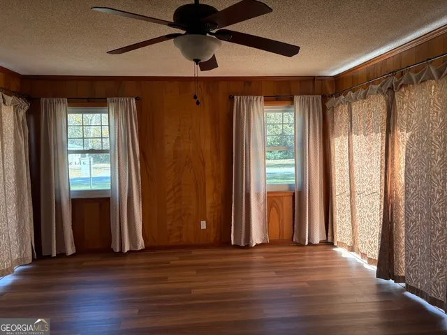 an empty room with wooden floor and windows with curtains