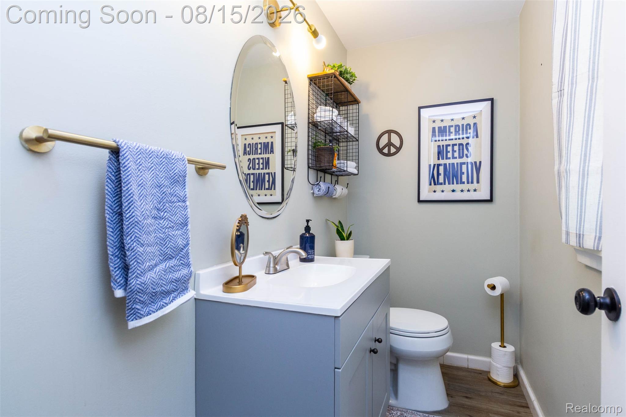 29604 Chelmsford Road Southfield, MI 48076 - Photo 26 of 39 Vanity with a white countertop and undermount sink, oval wall mirror, wall-mounted light fixture, and wood-finish flooring