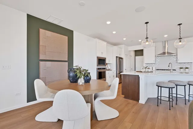 a kitchen with stainless steel appliances kitchen island granite countertop a dining table chairs and a refrigerator