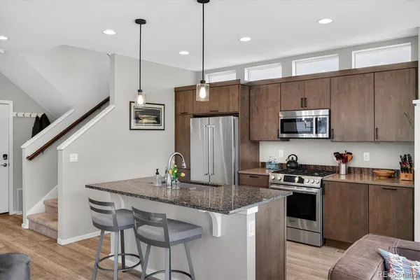 a kitchen with kitchen island granite countertop stainless steel appliances a sink a stove a refrigerator cabinets and wooden floor
