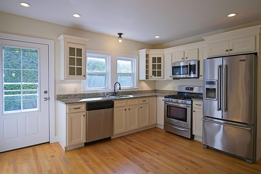 a kitchen with stainless steel appliances granite countertop a stove a sink dishwasher a refrigerator and a microwave oven with wooden floor