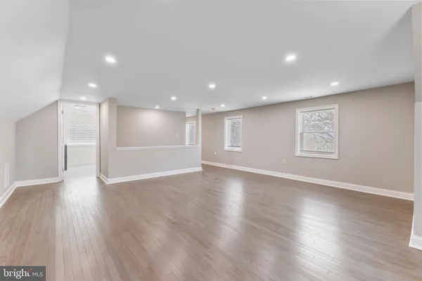 a view of an empty room with wooden floor kitchen view and a window