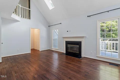 an empty room with wooden floor fireplace and windows