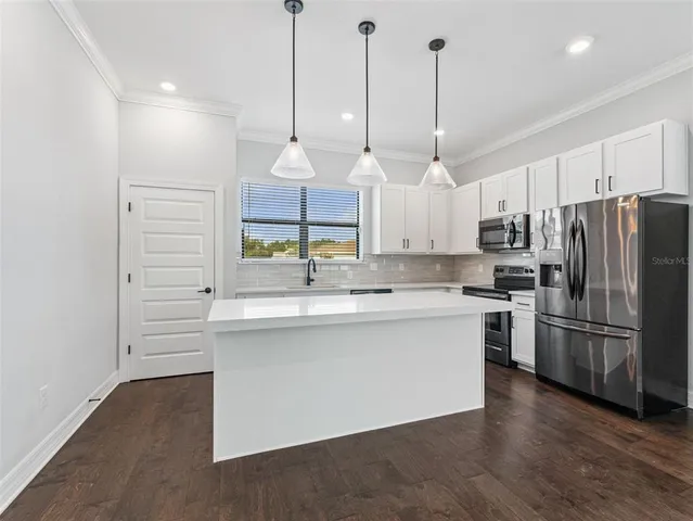 a large kitchen with kitchen island a stove a sink a center island a refrigerator and a wooden floor