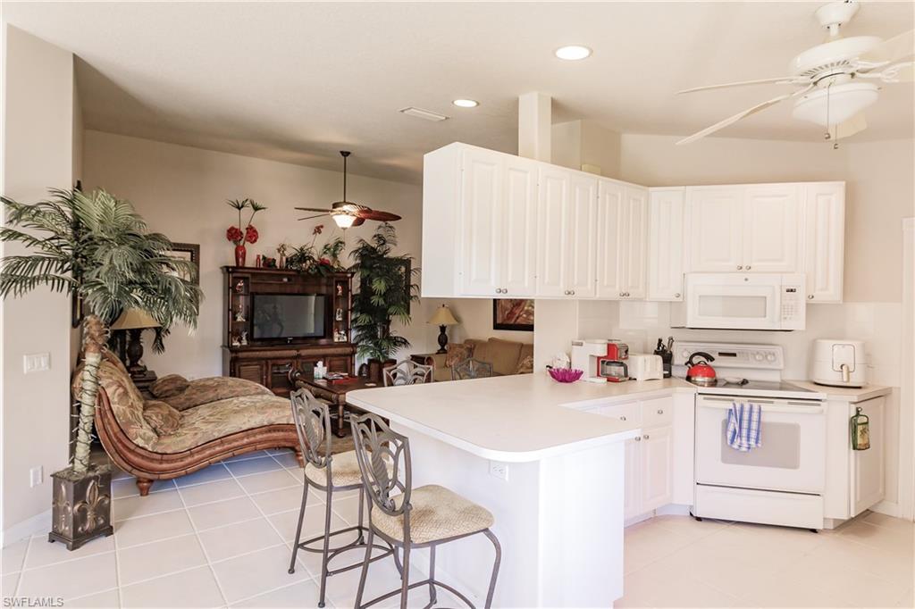 4113 Tabago Lane Naples, FL 34119 - Photo 19 of 50 Kitchen with kitchen peninsula, a kitchen bar, white appliances, white cabinets, and light tile patterned flooring