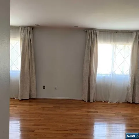 an empty room with wooden floor and windows with curtains