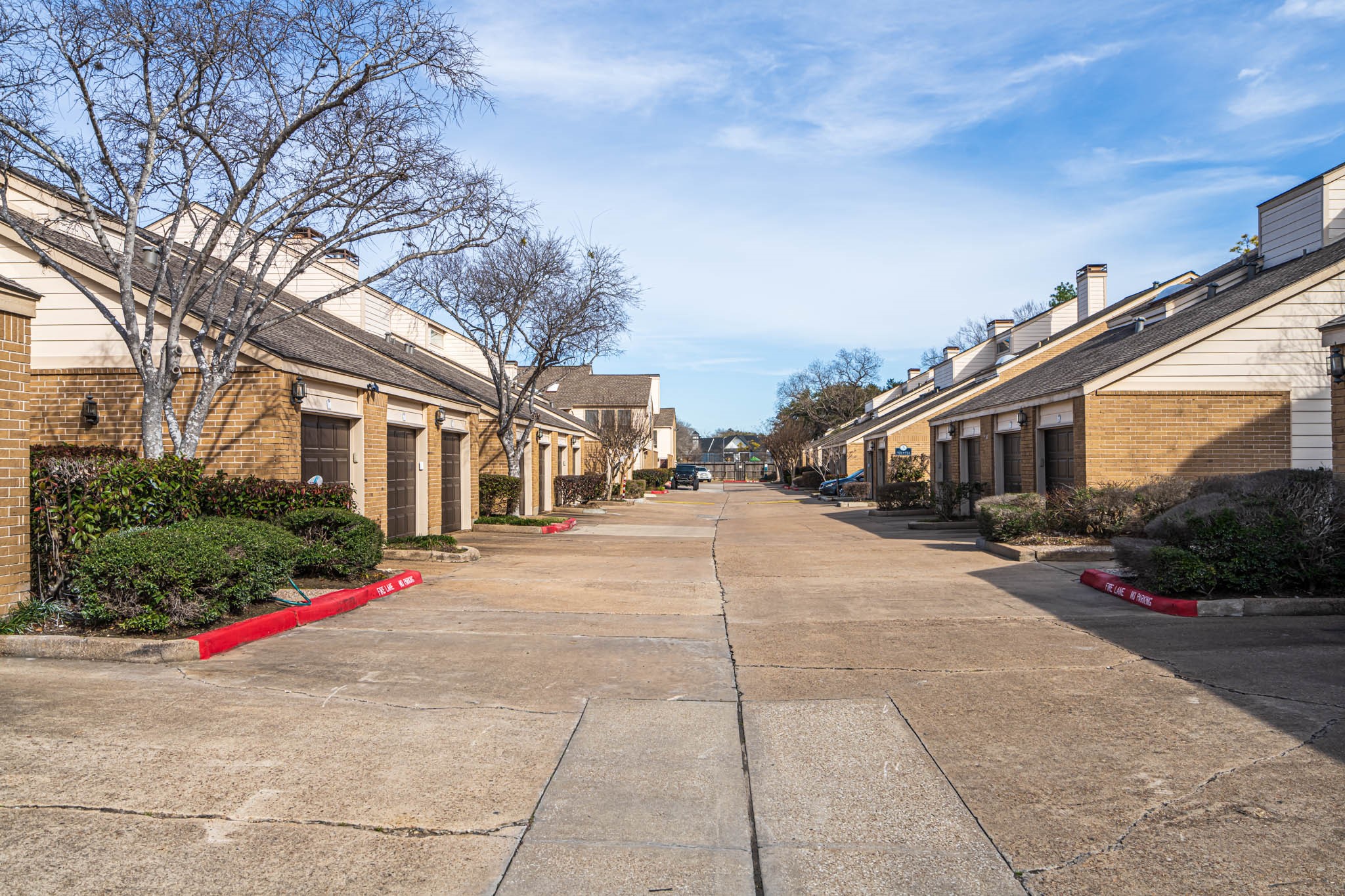 2277 South Kirkwood Road, Unit 4/808 Houston, TX 77077 - Photo 22 of 23 Quiet residential street lined with townhouses featuring brick facades and sloped roofs. The area is well-maintained, with trimmed shrubs and leafless trees, suggesting a peaceful suburban setting.