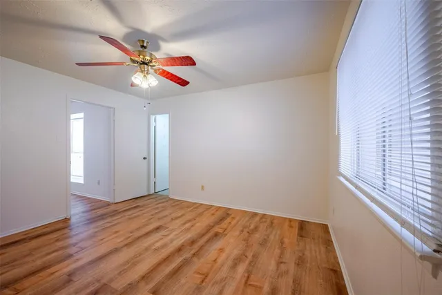 a view of an empty room with wooden floor and a ceiling fan
