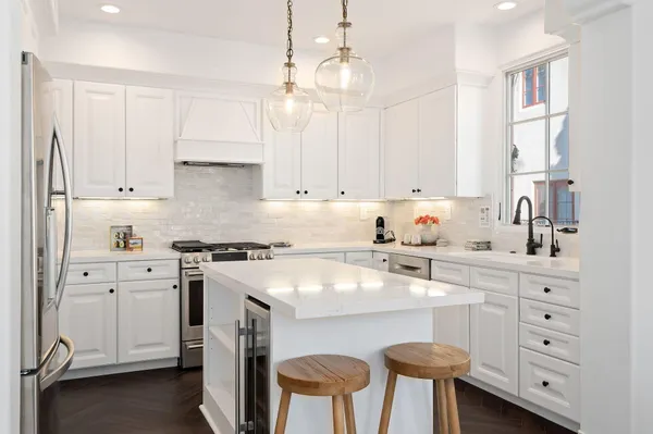 a kitchen with stainless steel appliances a stove a sink a refrigerator and white cabinets with wooden floor