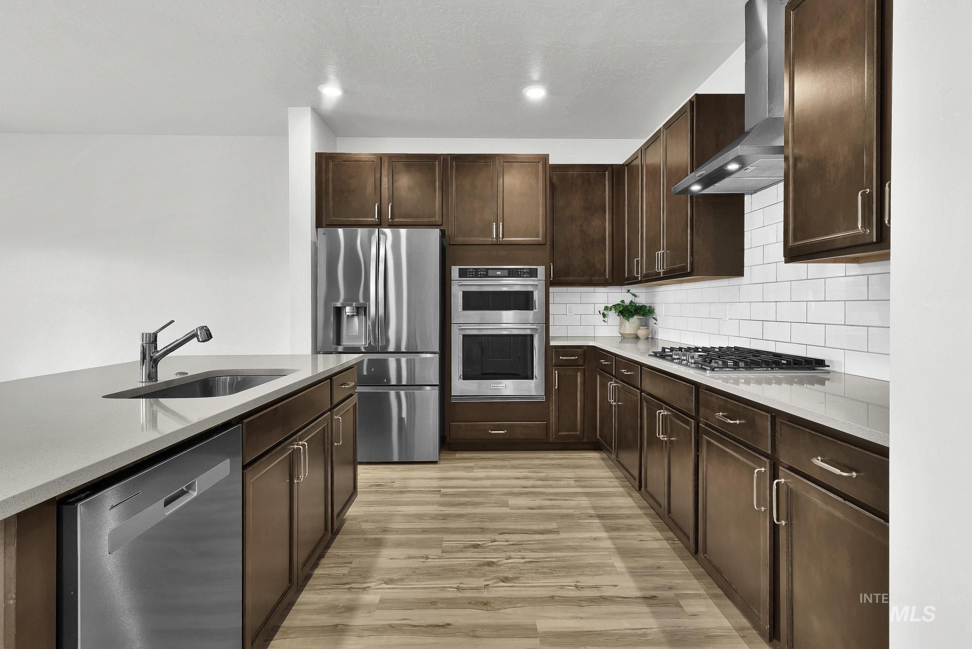 717 West Lyra Street Meridian, ID 83642 - Photo 11 of 50 Modern kitchen featuring rich wood-finish cabinetry, stainless steel appliances, light-toned countertops, and a subway tile backsplash