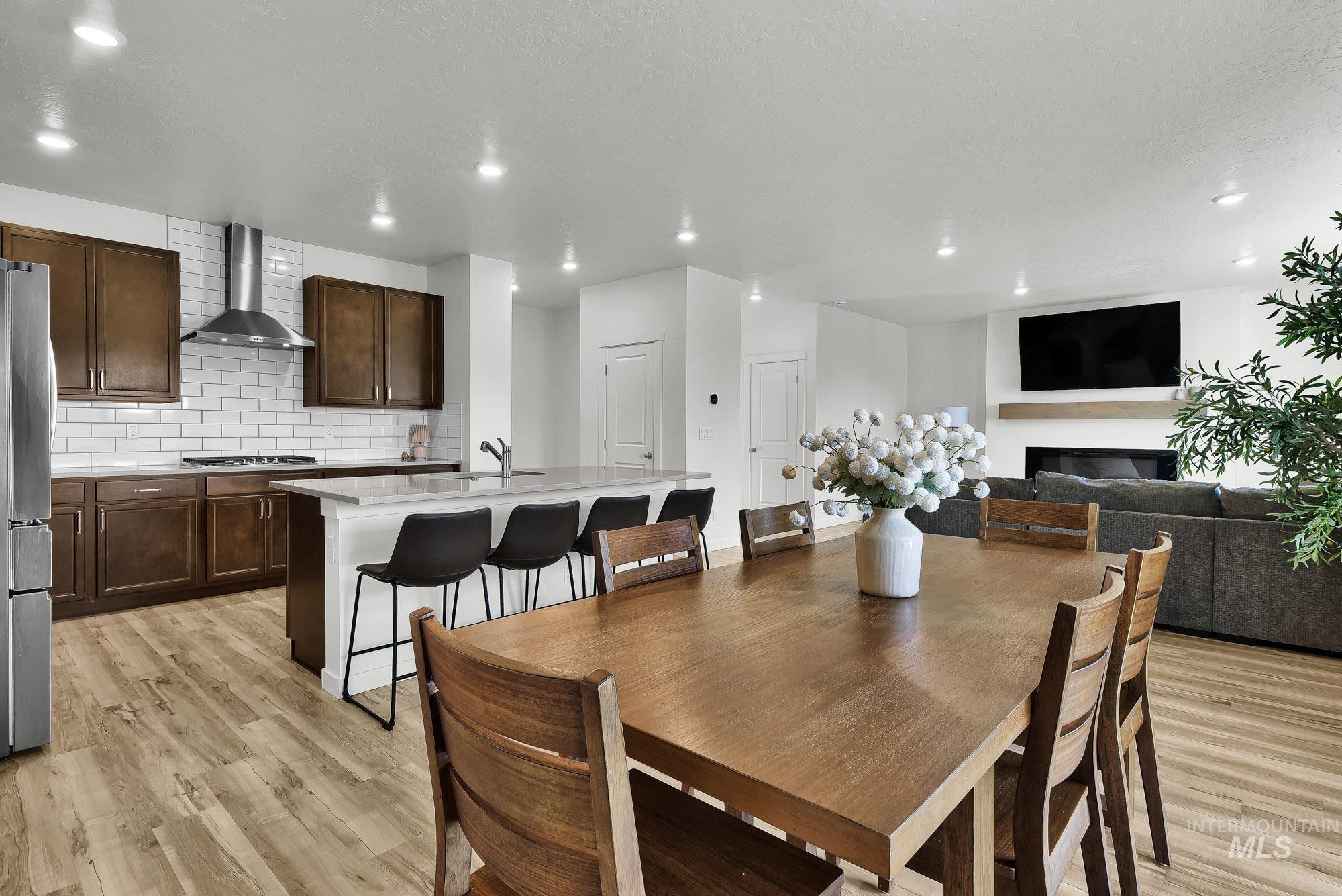 717 West Lyra Street Meridian, ID 83642 - Photo 12 of 50 Open-concept living space featuring wood-finish flooring, a kitchen island with seating, dark wood cabinetry, stainless steel appliances, and a modern fireplace with a mantel