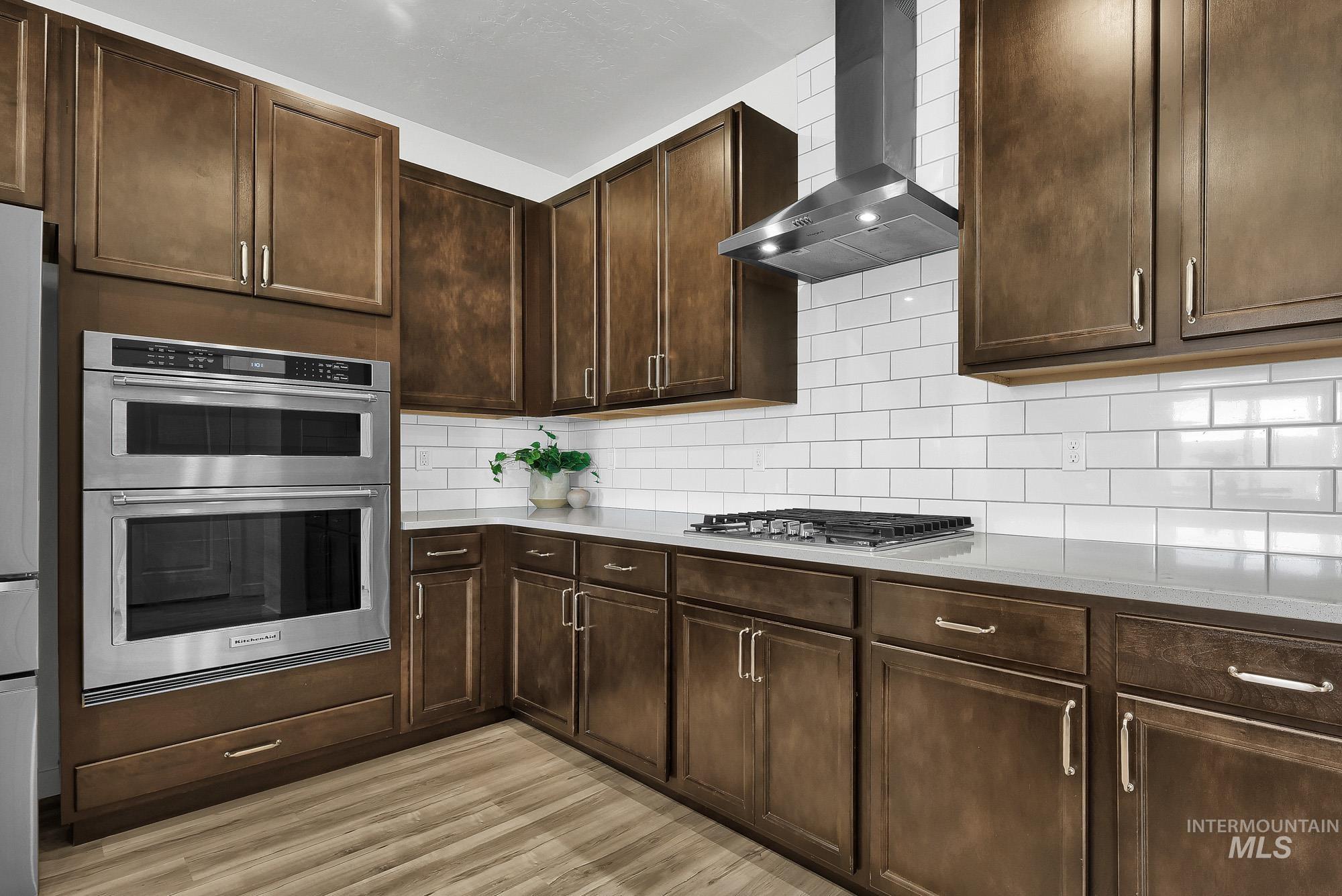 717 West Lyra Street Meridian, ID 83642 - Photo 14 of 50 Stainless steel double wall ovens, wood-finish flooring, white subway tile backsplash, gas cooktop, and an exhaust hood define this kitchen space