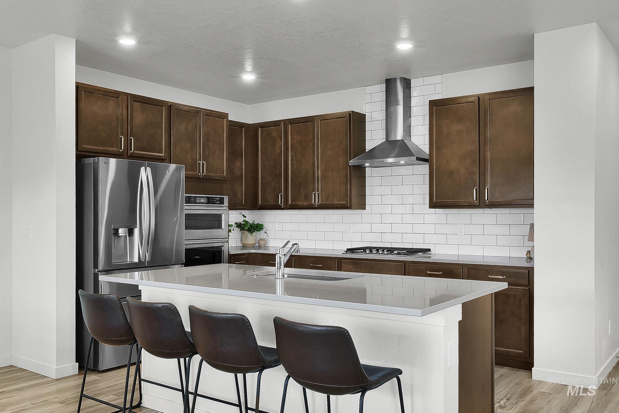717 West Lyra Street Meridian, ID 83642 - Photo 17 of 50 Contemporary kitchen featuring stainless steel appliances, dark wood-finish cabinetry, white subway tile backsplash, a center island with countertop seating, and wood-finish flooring