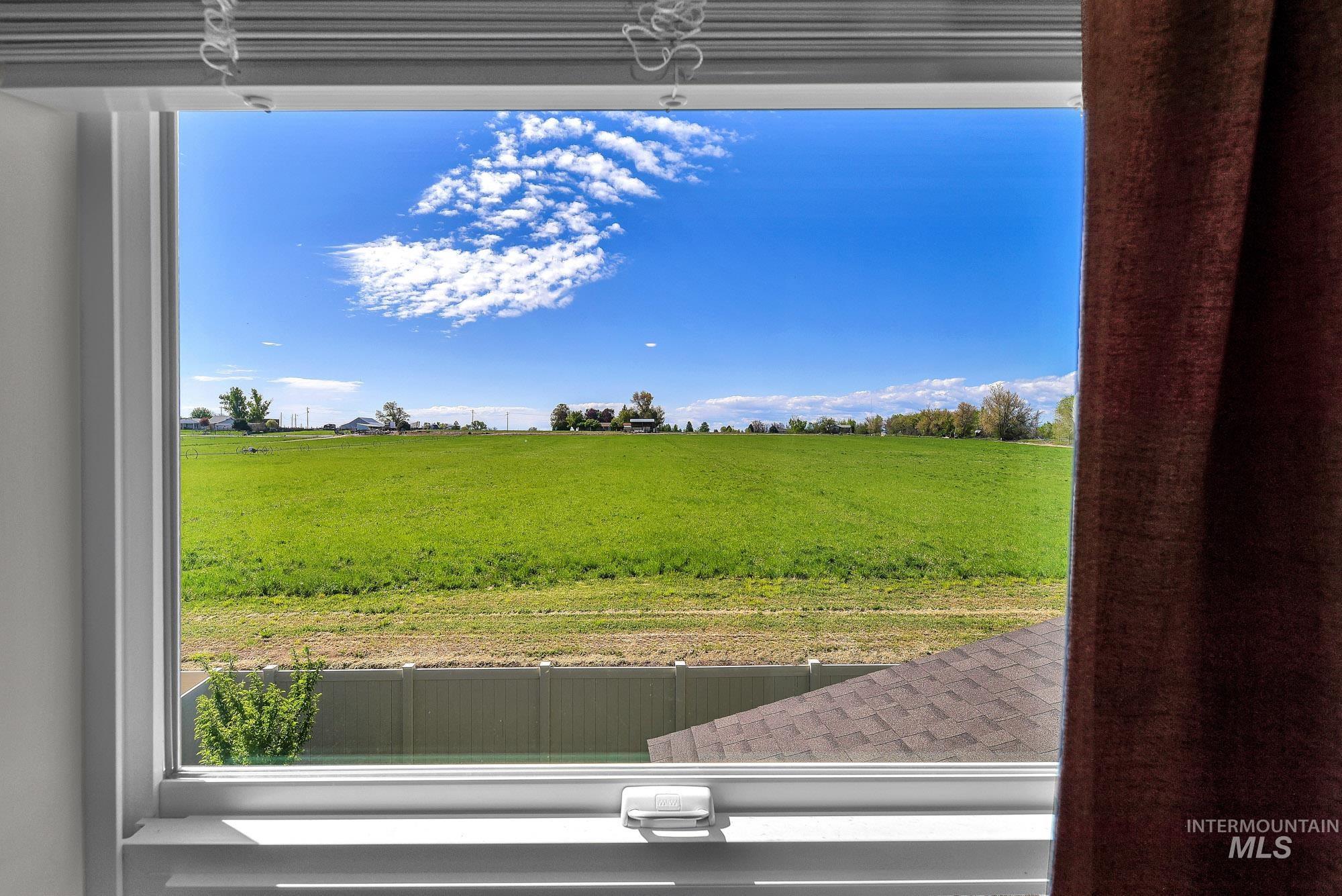 717 West Lyra Street Meridian, ID 83642 - Photo 27 of 50 Expansive green field visible through a window with white trim, featuring a clear blue sky with scattered clouds