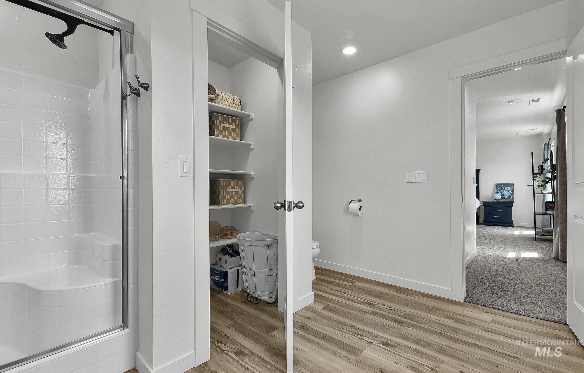 717 West Lyra Street Meridian, ID 83642 - Photo 33 of 50 Bathroom featuring a glass-enclosed shower with white tiled walls and built-in bench, wood-finish flooring, recessed lighting, and a linen closet with multiple shelving units