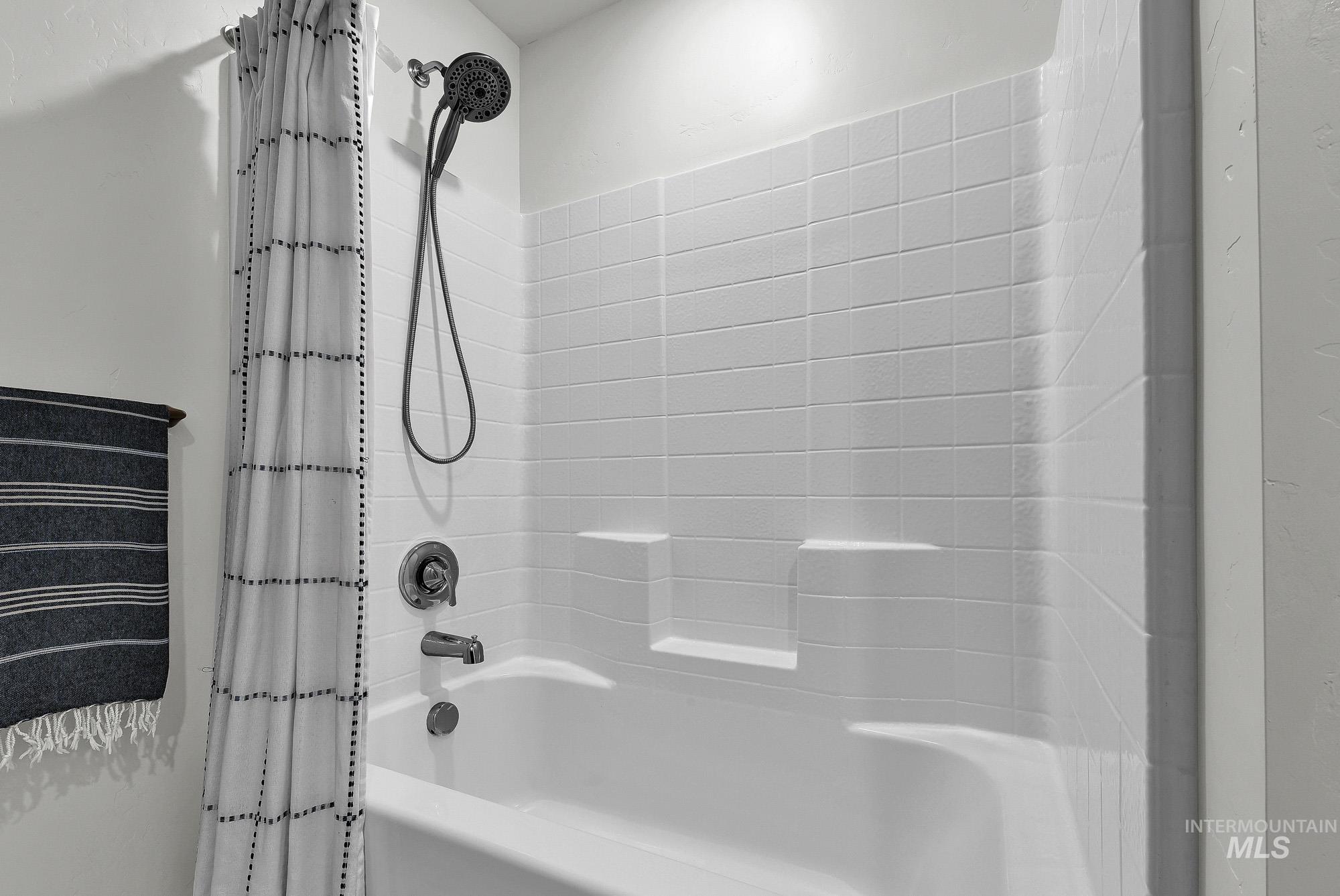 717 West Lyra Street Meridian, ID 83642 - Photo 43 of 50 White bathtub with an integrated tiled shower surround, featuring a handheld showerhead and dual-lever faucet in a brushed nickel finish