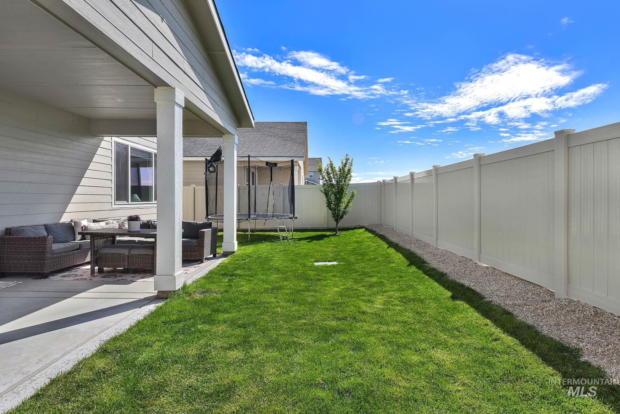 717 West Lyra Street Meridian, ID 83642 - Photo 46 of 50 Backyard featuring a covered patio with concrete flooring, a manicured lawn, a gravel border, a young deciduous tree, and a tall white privacy fence