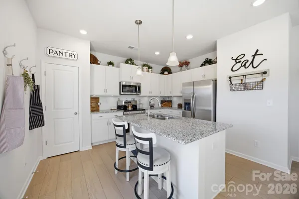 a kitchen with stainless steel appliances granite countertop a refrigerator a sink dishwasher a stove and white cabinets with wooden floor