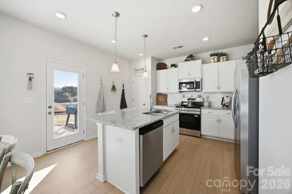 a kitchen with granite countertop a sink stove a refrigerator and white cabinets with wooden floor