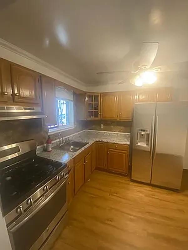 Kitchen with light wood finished floors, under cabinet range hood, brown cabinetry, stainless steel appliances, and a sink