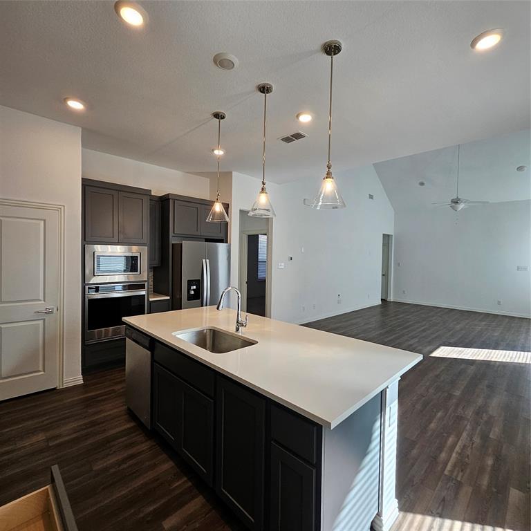 Kitchen featuring dark wood-finish flooring, a central island with an undermount sink and light-toned countertop, dark cabinetry, and stainless steel appliances