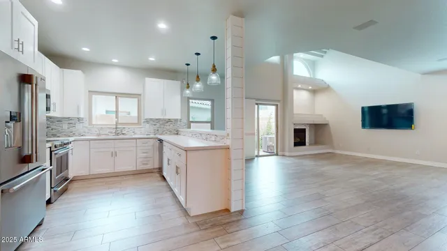 a large kitchen with stainless steel appliances kitchen island granite countertop a stove a sink a refrigerator and white cabinets with wooden floor