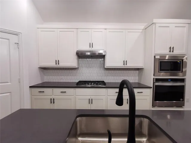a kitchen with granite countertop a stove a microwave a sink and white cabinets