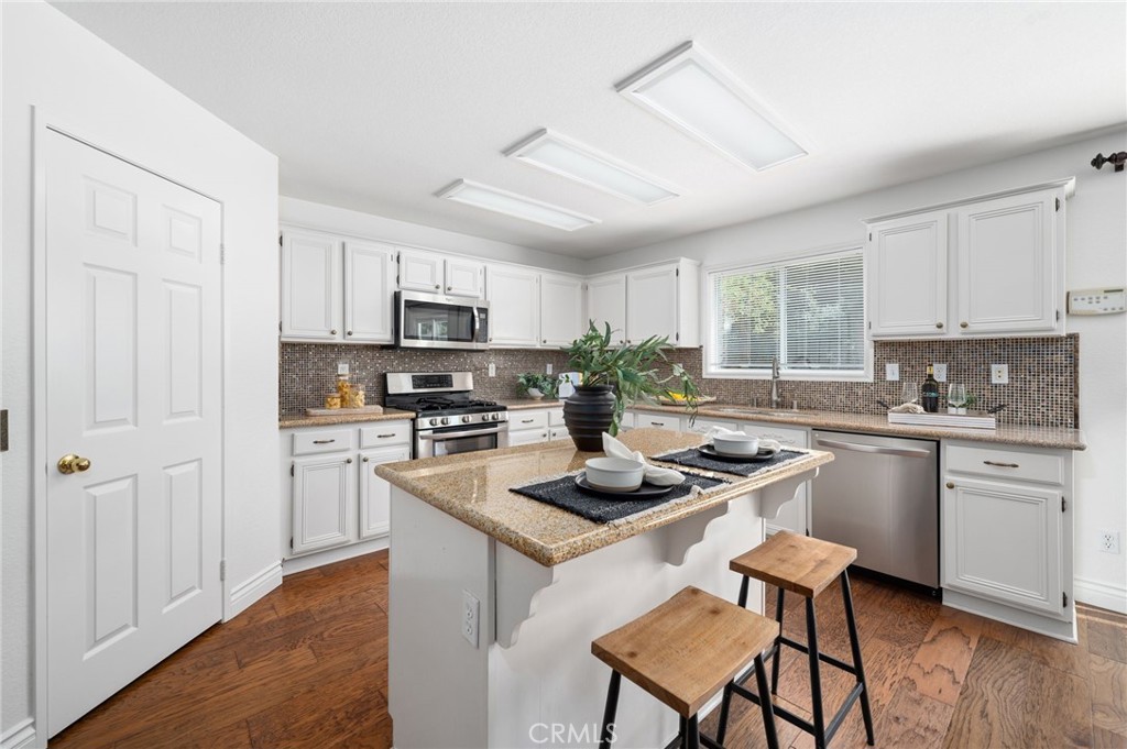 33751 Abbey Road Temecula, CA 92592 - Photo 10 of 41 a kitchen with stainless steel appliances kitchen island granite countertop a stove a sink dishwasher a refrigerator and white cabinets with wooden floor