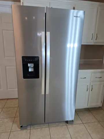 a view of a refrigerator in kitchen and an empty room with wooden floor
