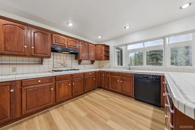 a kitchen with stainless steel appliances granite countertop wooden cabinets a sink and dishwasher a stove with wooden floors