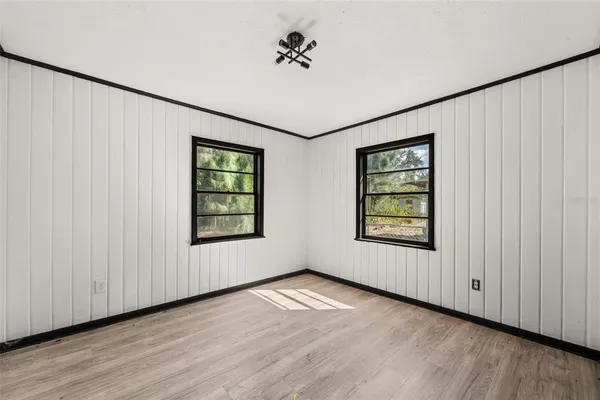 an empty room with wooden floor chandelier fan and windows
