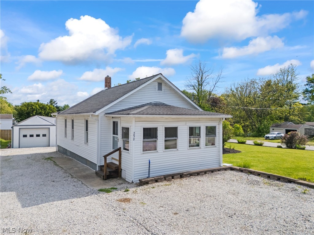 258 Randolph Road Mogadore, OH 44260 - Photo 1 of 49 White siding residence featuring a sunroom, gravel parking area, and a detached two-car garage