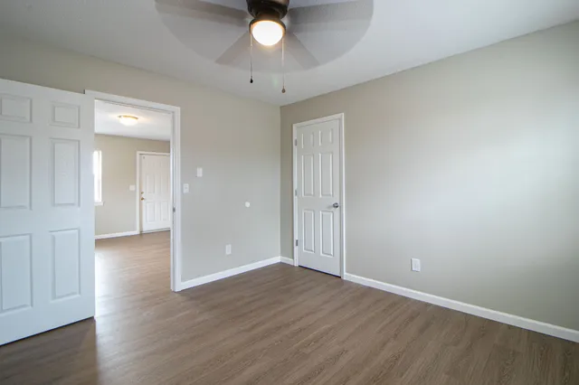 a view of an empty room with wooden floor and a chandelier fan