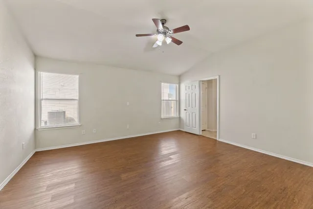 an empty room with wooden floor fan and windows