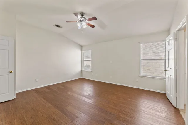 an empty room with wooden floor chandelier fan and windows