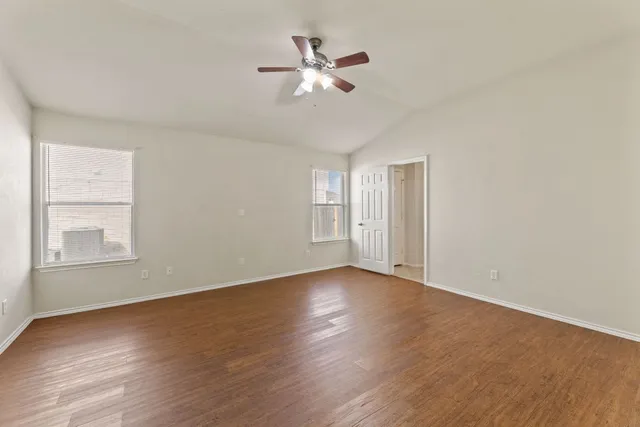 a view of an empty room with wooden floor and a ceiling fan