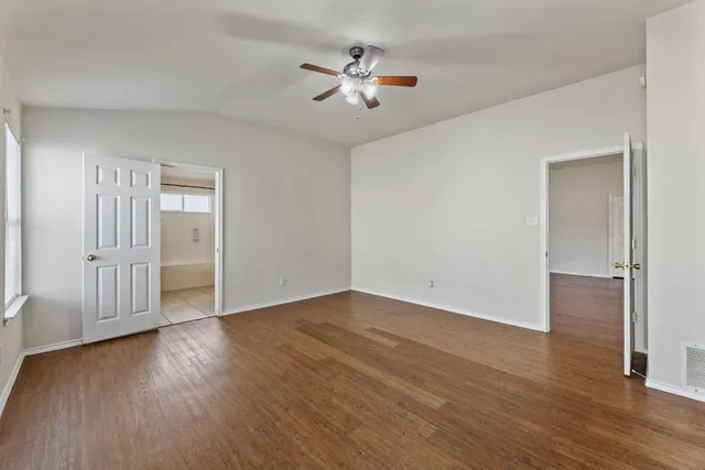 an empty room with wooden floor ceiling fan and windows