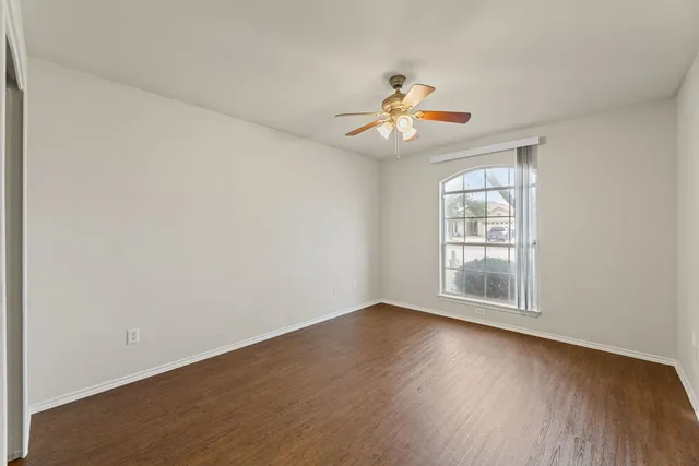 an empty room with wooden floor chandelier fan and windows