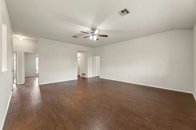 a view of an empty room with chandelier fan and wooden floor