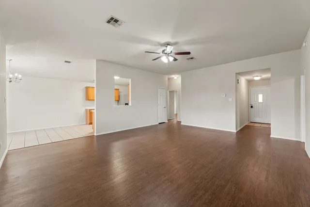 a view of an empty room with wooden floor and a ceiling fan