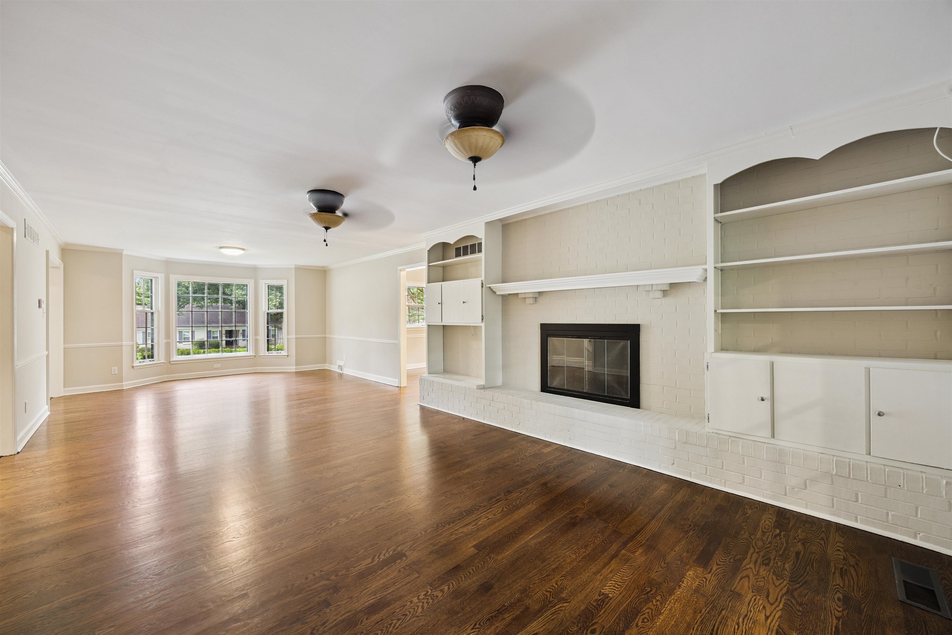 2030 Brierbrook Road Germantown, TN 38138 - Photo 4 of 16 Unfurnished living room featuring dark wood-style floors, built in features, a brick fireplace, a ceiling fan, and ornamental molding