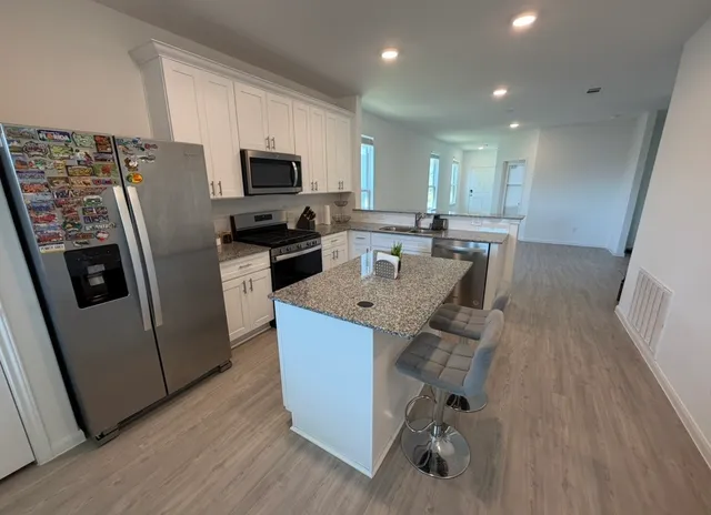 a kitchen with stainless steel appliances granite countertop a refrigerator oven a sink dishwasher and white cabinets with wooden floor