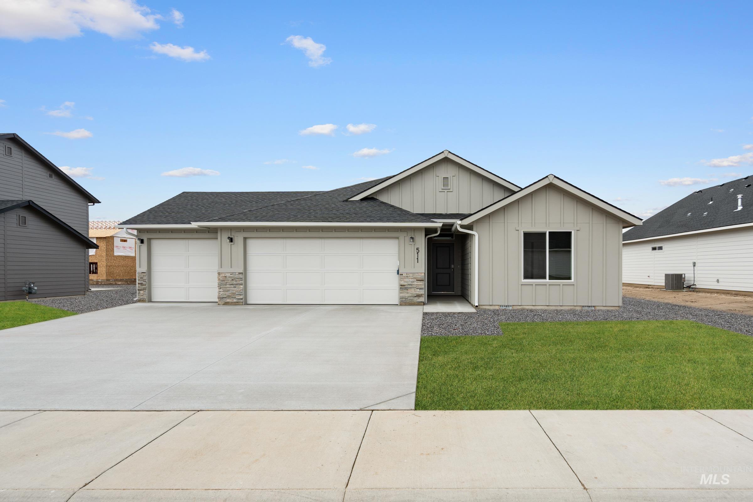 Single story home with an attached garage, board and batten siding, concrete driveway, a front lawn, and stone siding