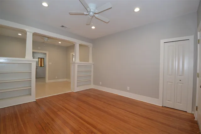 an empty room with wooden floor closet and windows