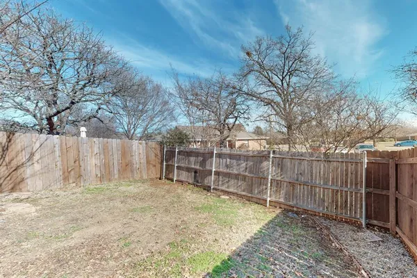 a view of a backyard with wooden fence and large trees
