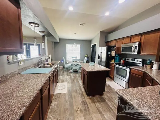 a large kitchen with stainless steel appliances granite countertop a stove top oven a sink dishwasher a dining table and chairs with wooden floor