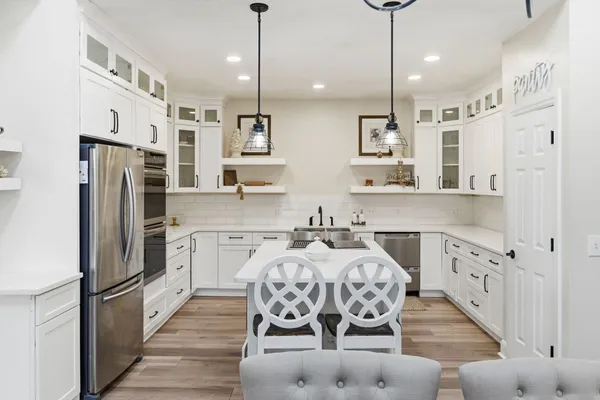 a kitchen with stainless steel appliances kitchen island granite countertop a refrigerator a stove a oven and white cabinets with wooden floor