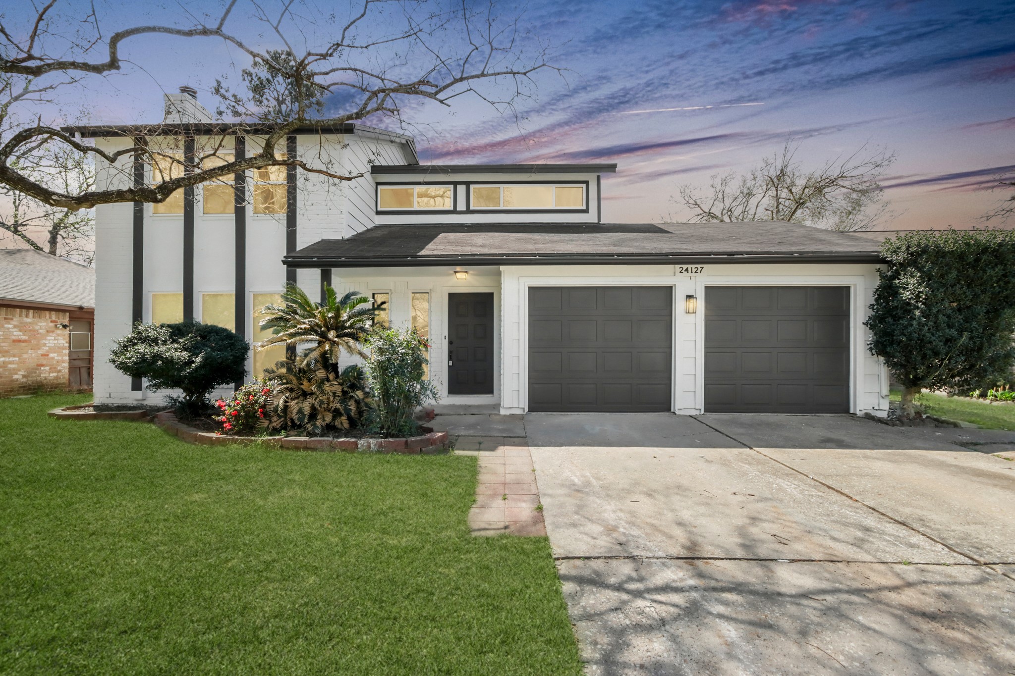 Striking curb appeal welcomes you with clean modern lines, a spacious driveway, and a two-car garage, all framed by a generous front lawn and mature landscaping.